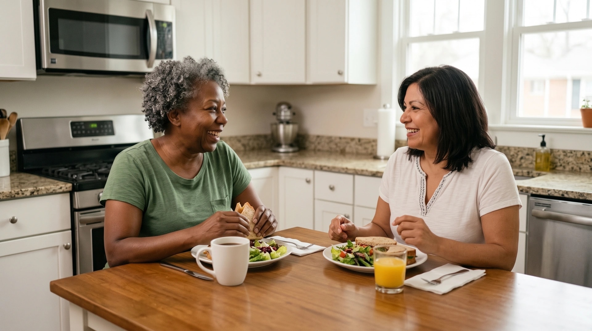Two women laughing together over a healthy lunch at a kitchen table