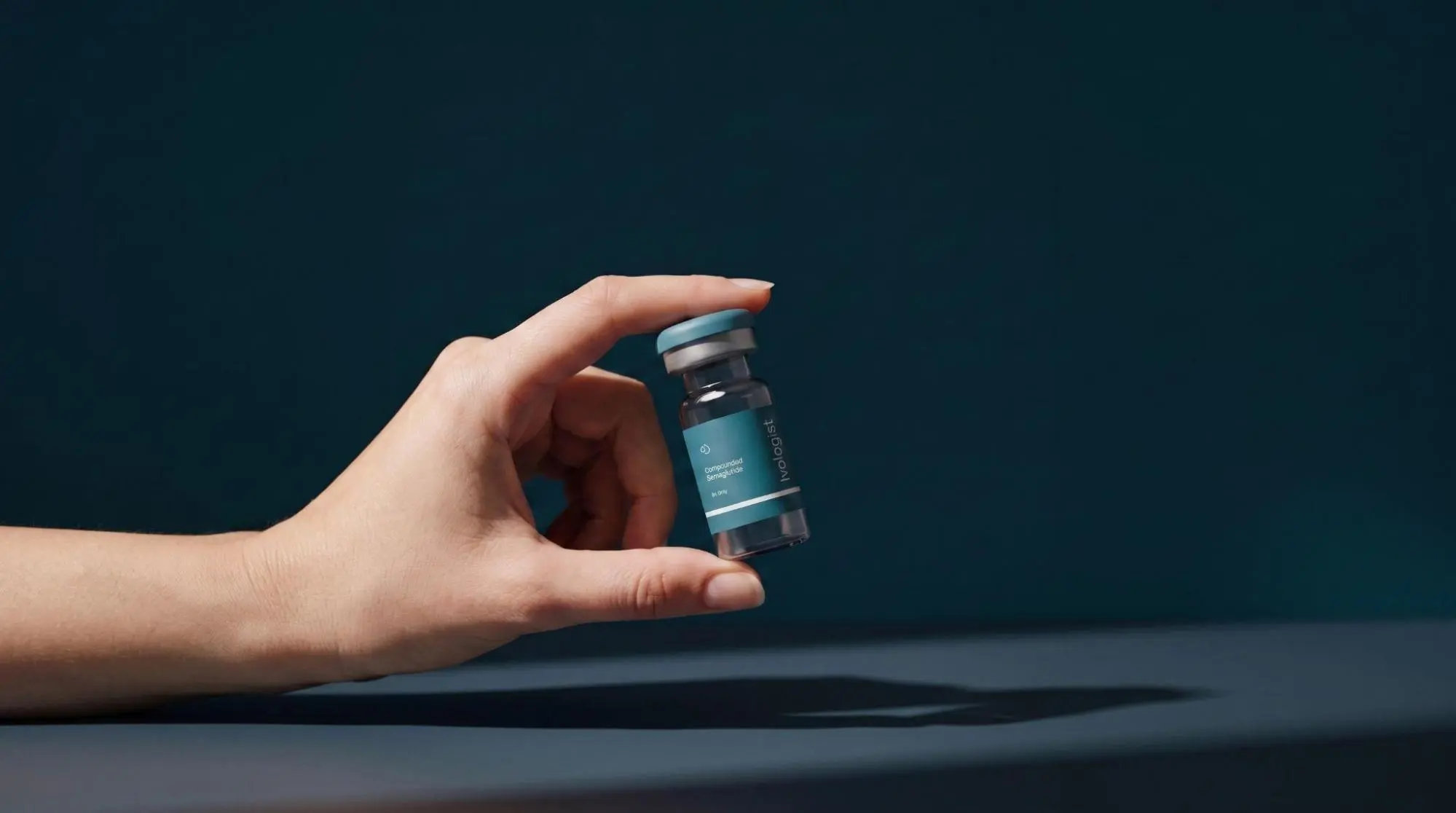 A hand holding a small glass vial of compounded semaglutide against a dark background