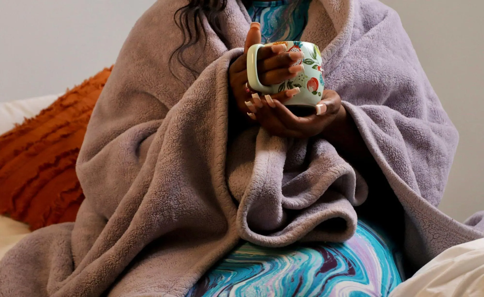 Person wrapped in a cozy purple blanket holding a warm mug