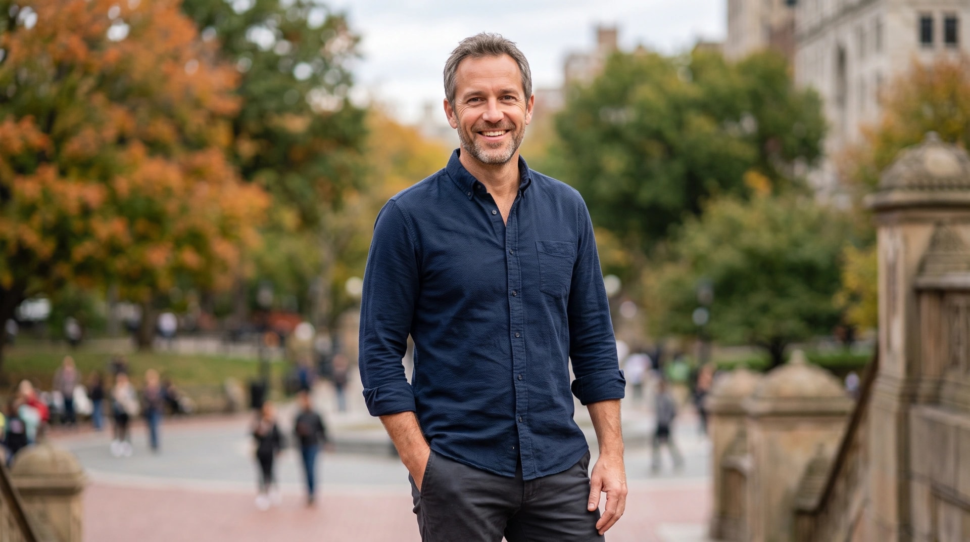 A smiling man standing on a tree-lined path in the fall