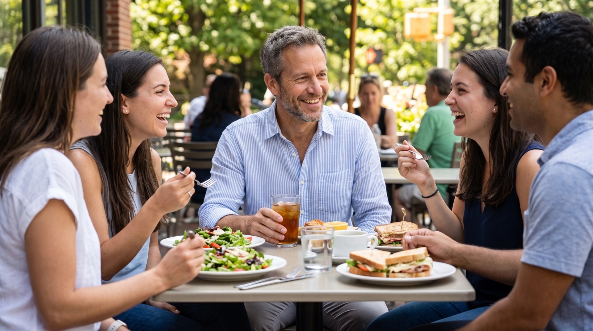 A man sharing lunch and laughing with friends at an outdoor table