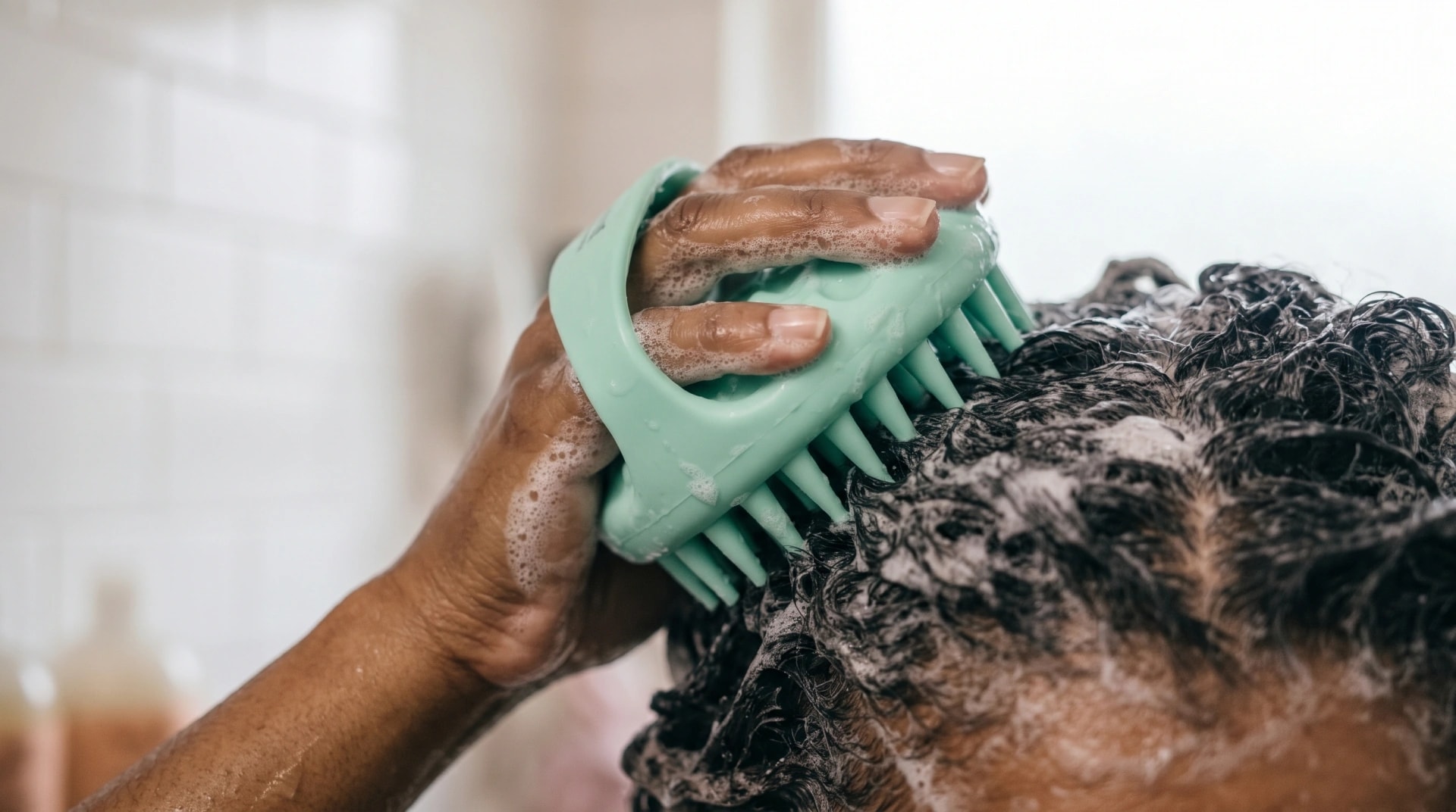 A silicone scalp brush being worked through lathered curly hair