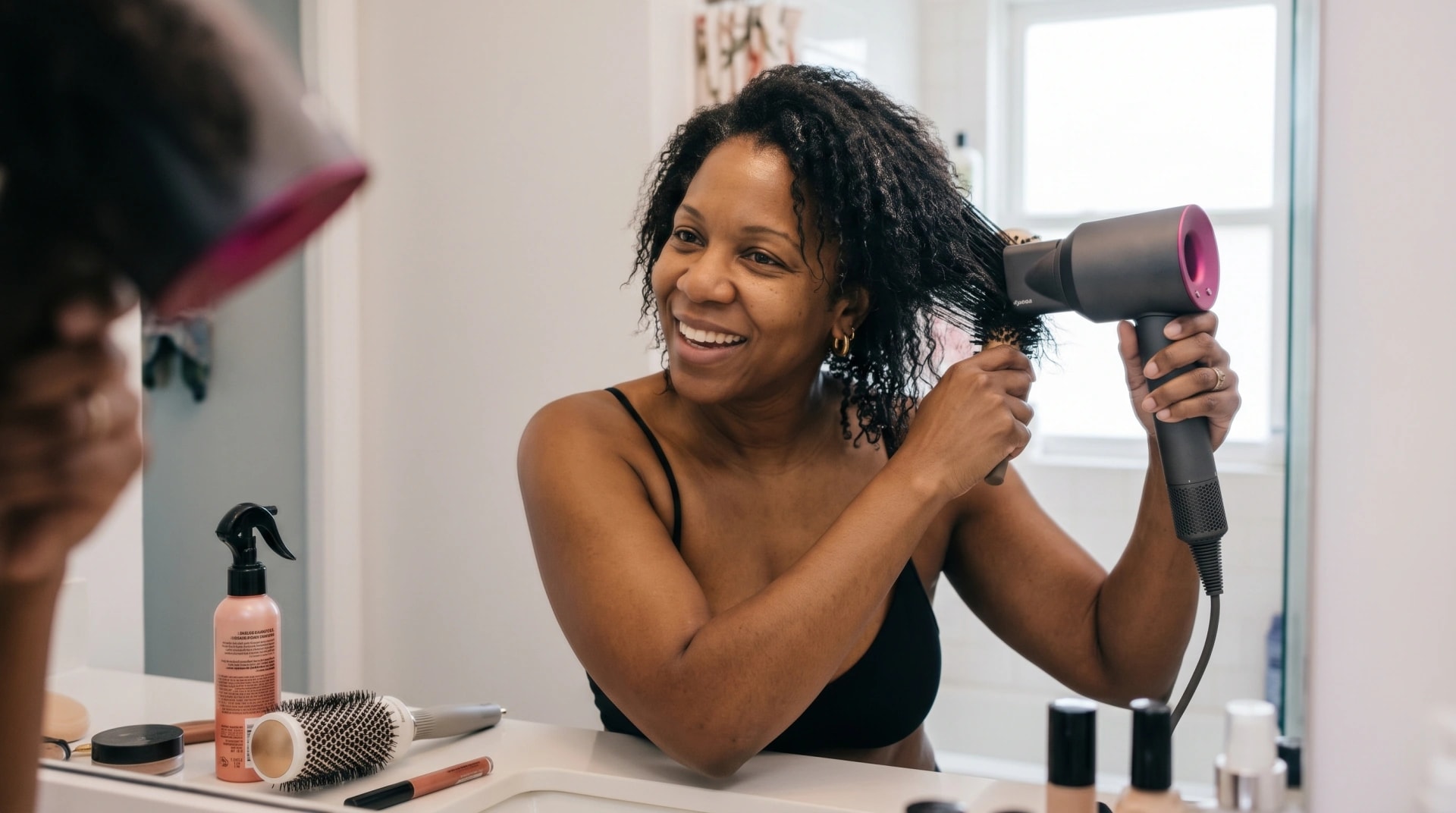A woman blow-drying her curly hair in front of a mirror after washing