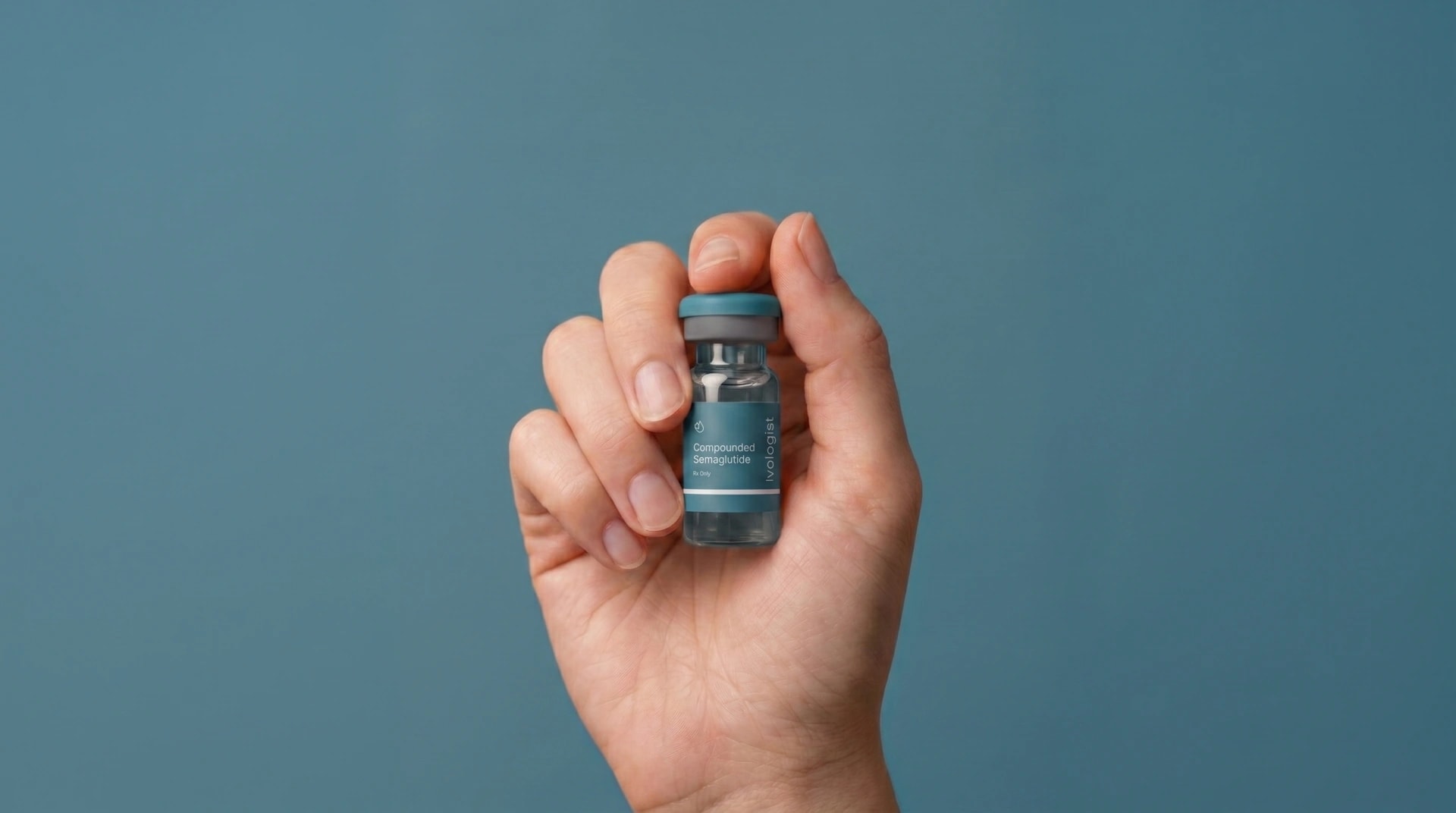 A hand holding a small medication vial against a teal background