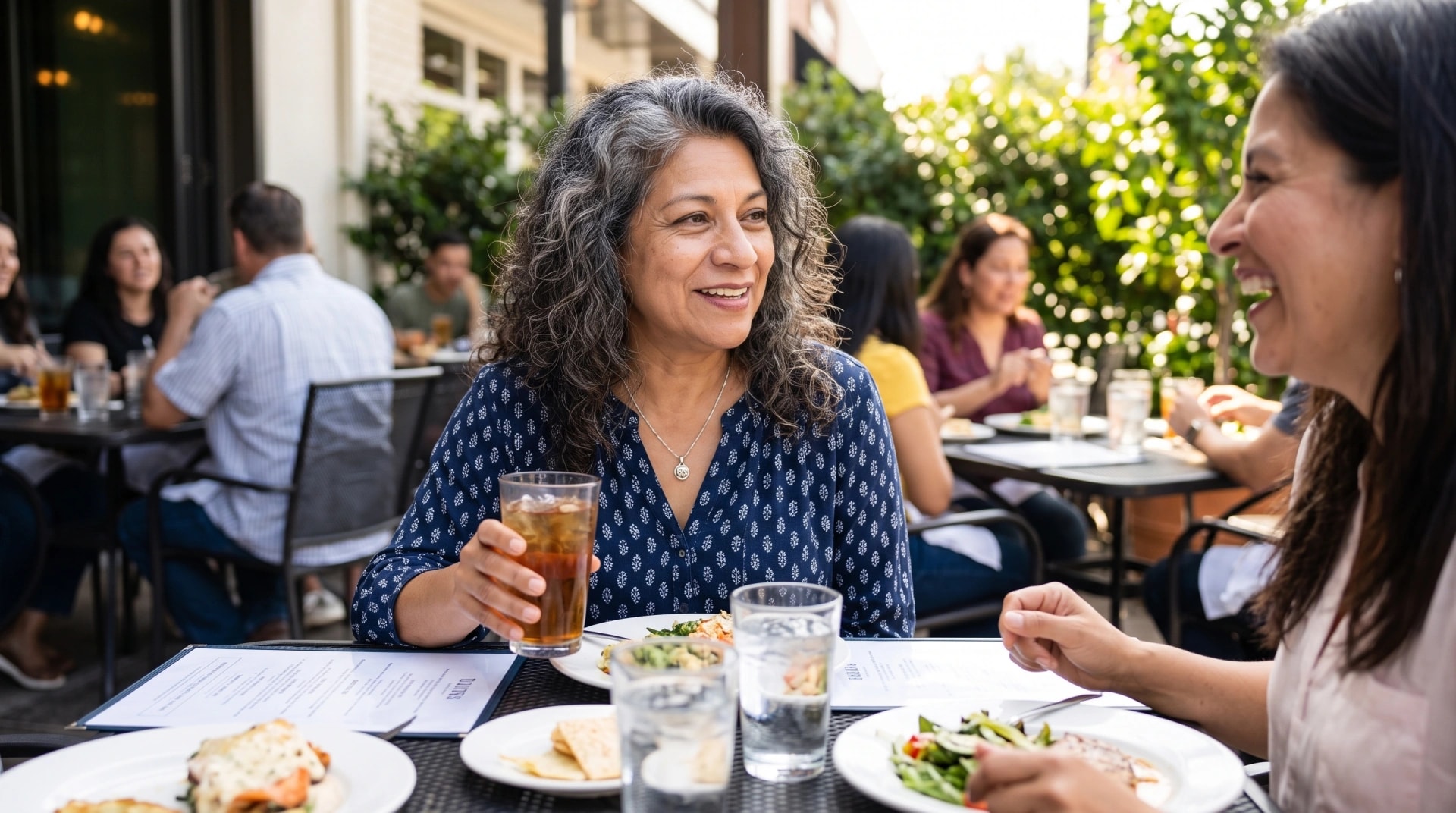 A woman laughing with a friend over lunch on a restaurant patio