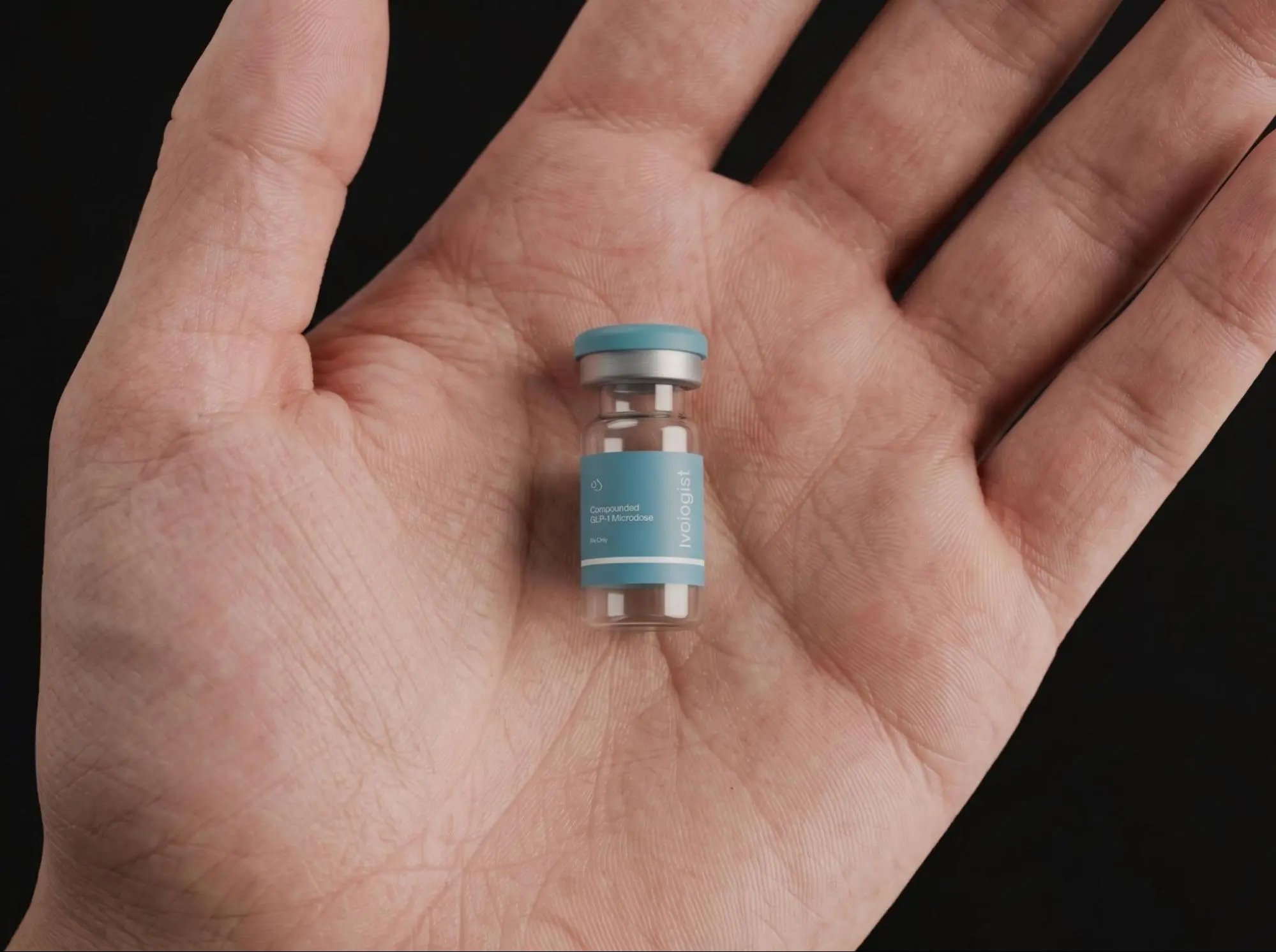A hand holding a small vial of compounded GLP-1 medication