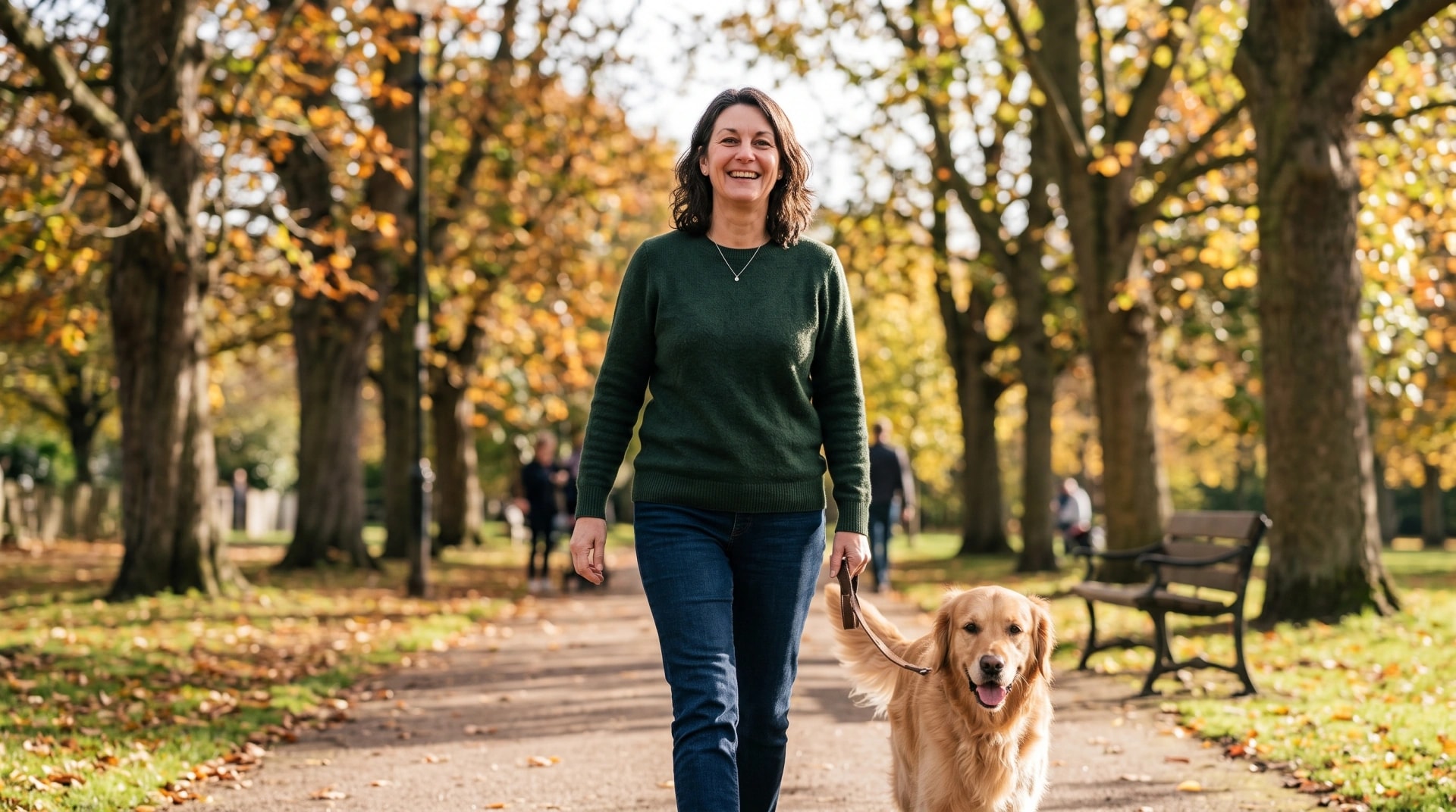 A woman walking her golden retriever along an autumn park path